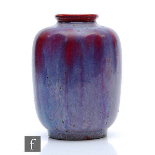 81 - Ruskin Pottery - A small high fired vase of barrel form with a roll rim neck decorated with a lavend... 