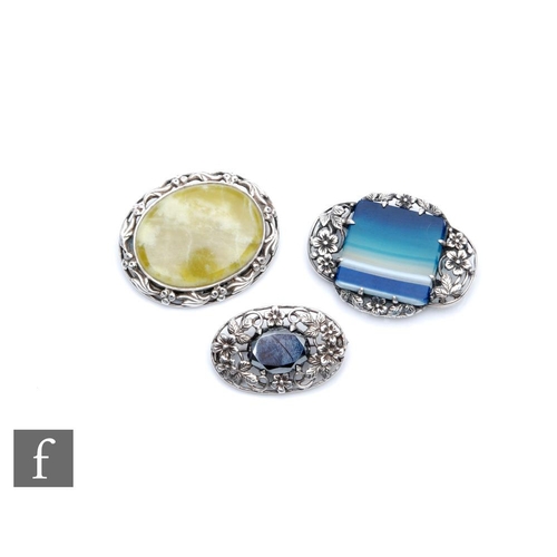 410 - Three Arts and Crafts style brooches, each set with a central polished hardstone within a silver mou... 