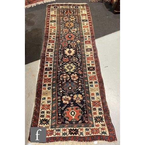 1280 - A mid 20th Century Kazak runner, the rug with repeat pattern medallions on a dark blue ground within... 