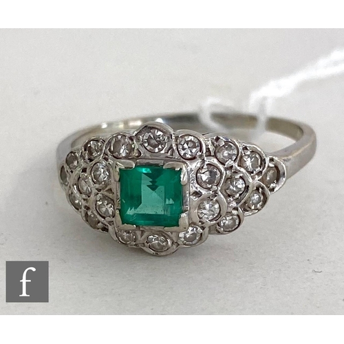 145 - An 14ct white gold emerald and diamond cluster ring, central square cut emerald to an oval diamond e... 