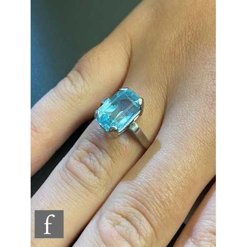 142 - An 18ct white gold single stone aquamarine ring, claw set emerald cut stone to scrolled shoulders, w... 