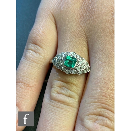 145 - An 14ct white gold emerald and diamond cluster ring, central square cut emerald to an oval diamond e... 