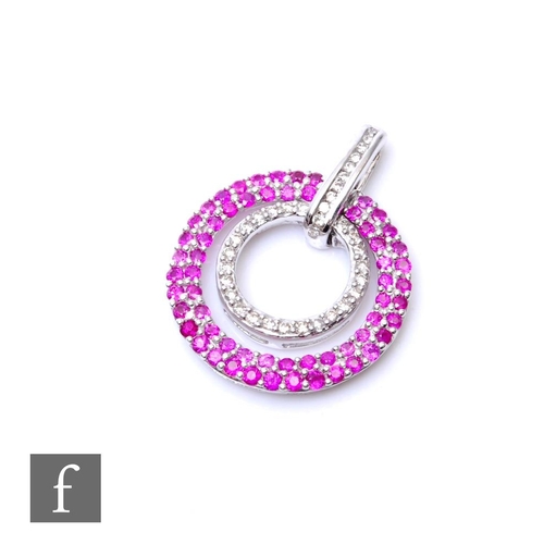 679 - A 9ct hallmarked white gold ruby and diamond circular pendant, a double row of rubies encompassing a... 