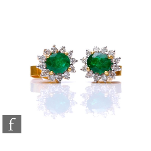 702 - A pair of 18ct emerald and diamond stud earrings, central oval emerald within twelve stone brilliant... 