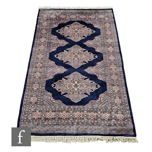 1111 - Two contemporary Bokhara rugs, each decorated with diamond shaped medallions on a dark blue ground, ... 