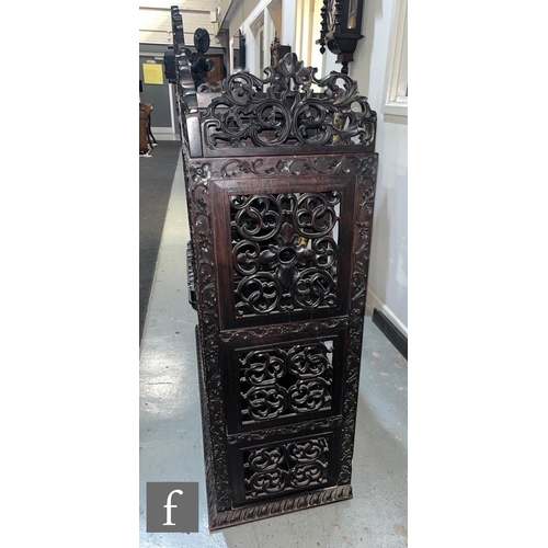 1094 - A late 19th Century Anglo Indian carved harwood/Padouk floorstanding cabinet, the pierced top rail o... 