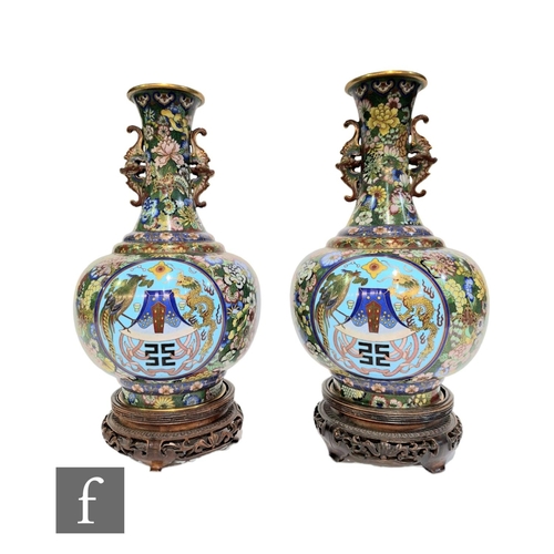 A pair of Chinese cloisonne vases, each of bottle form, rising to a slender neck applied with cicada handles, the body of each with roundels filled with dragons, birds and auspicious characters, before a densely decorated ground, height 30cm, on wooden stands. (2)