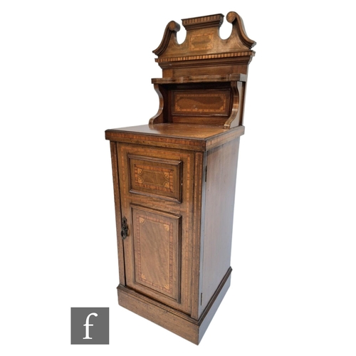 603 - An Edwardian satinwood banded and inlaid bedside cupboard enclosed by a panel door below a broken sw... 