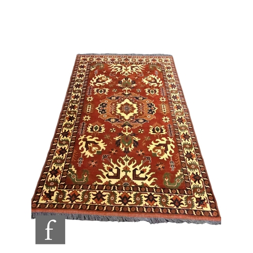 565 - A Kazak style rug central medallion and stylised hooked design on a deep red ground, 244cm x 168cm.