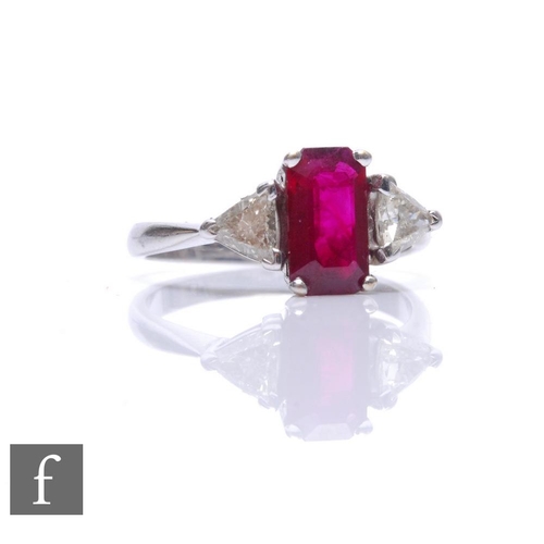 An 18ct hallmarked ruby and diamond three stone ring, central emerald cut ruby, length 9.5mm, flanked by a trillion cut diamond to each shoulder, weight 4.5g, ring size P.