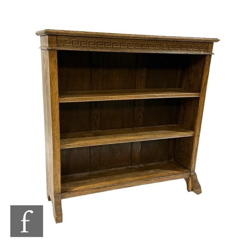 512 - A 1930s oak open three tier bookcase, adjustable shelves below a Greek Key frieze on splayed ends su... 