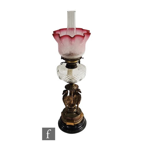 202 - A Victorian brass oil lamp, the cut glass reservoir over a base supported by three winged Griffins w... 