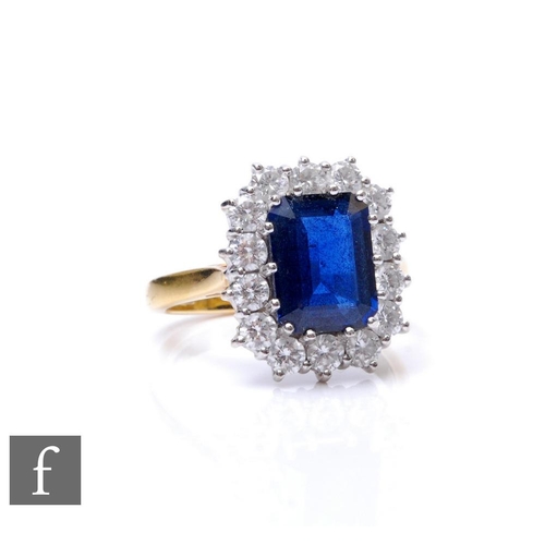 An 18ct hallmarked sapphire and diamond cluster ring, emerald cut sapphire, weight 3.36ct, within a border of fourteen brilliant cut diamonds, total weight approximately 1.00ct, weight 9.4g, ring size R.