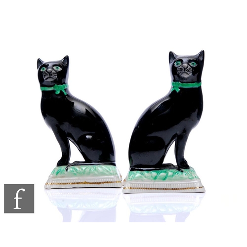 827 - A pair of late 19th Century Staffordshire pottery cats, each black with green eyes and seated on mou... 