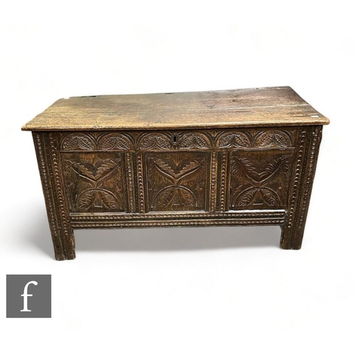 492 - An 18th Century carved oak coffer, the plank top over a triple panel leaf and lunette decorated fron... 