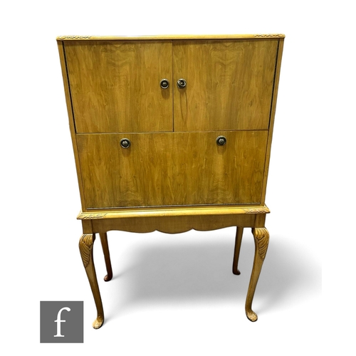 1005 - A Queen Anne style walnut cocktail cabinet, mirrored back enclosed by two doors over a fall, on carv... 