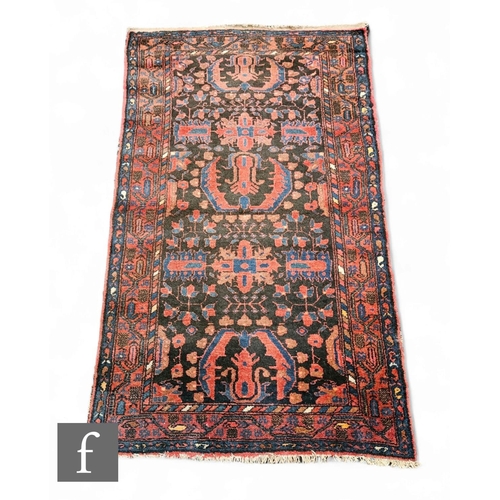 1065 - A Caucasian rug, four stylised hooked motifs within boteh border on a deep black, red and blue groun... 