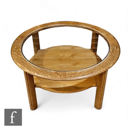 438 - A G-Plan ash coffee table of circular from, raised on four block supports, the glass inset top above... 