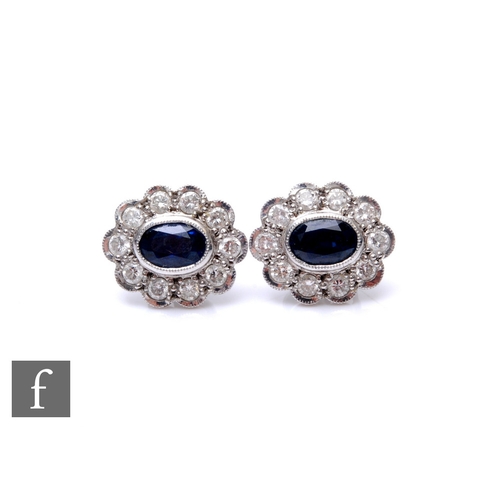 177 - A pair of 18ct white gold sapphire and diamond cluster earrings, central oval sapphires within a bor... 