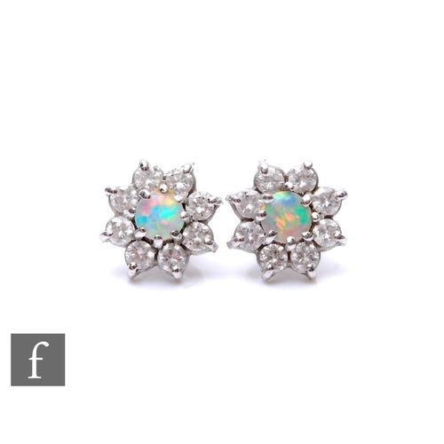 99 - A pair of 9ct white gold opal and diamond cluster stud earrings, central opal within a border of eig... 