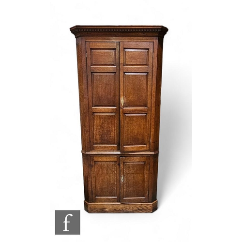 817 - A George III oak floorstanding corner cupboard, the fitted shaped shelf interior enclosed by a pair ... 