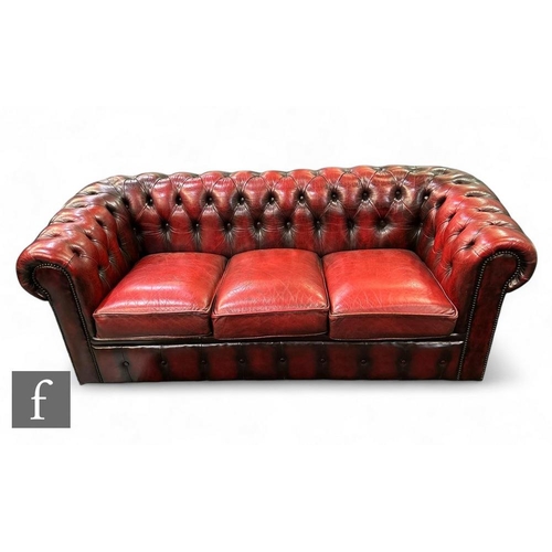 834 - An ox blood colour leather three seater buttoned back Chesterfield settee, three slip in cushions, l... 