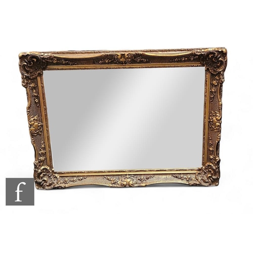 851 - A 20th Century bevel edged rectangular wall mirror within a scroll moulded edge border, 80cm x 110cm... 