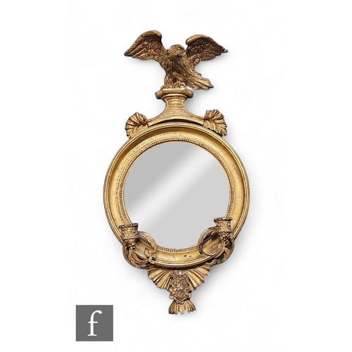 862 - A Regency circular gilt convex mirrored girandole, surmounted with a winged eagle over twin branched... 