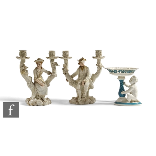 75 - A pair of late 19th Century Royal Worcester figural twin branch candelabrum, modelled as a seated co... 