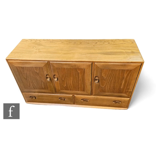 697 - A small Ercol light elm sideboard enclosed by a pair of cupboard doors above two short drawers, on s... 