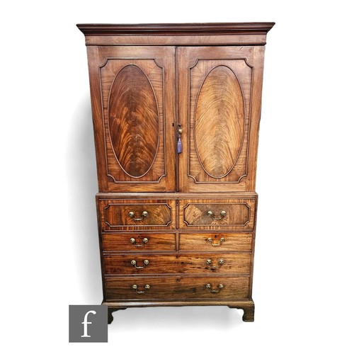 635 - A George III mahogany secretaire linen press, the converted hanging space enclosed by a pair of oval... 