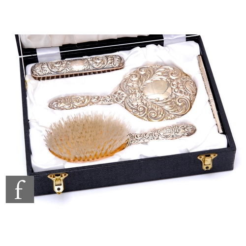 55 - A cased hallmarked silver backed four piece dressing table set each piece with embossed foliate deco... 