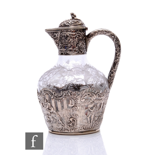 12 - A 19th Century continental silver and clear glass small claret jug with embossed figures to a landsc... 