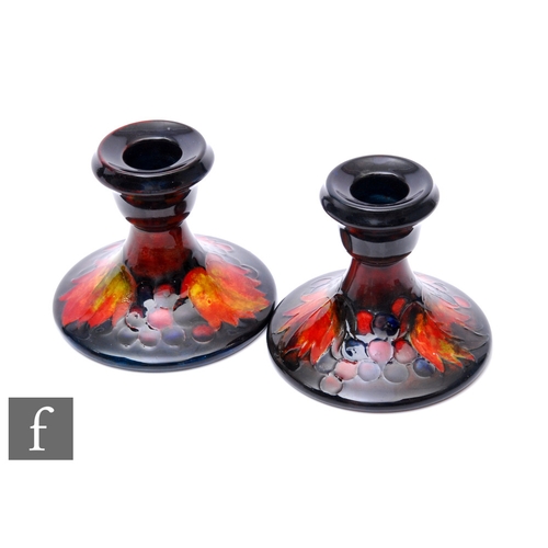 95 - William Moorcroft - Moorcroft Pottery - A pair of Flambe Leaf and Berry candlesticks, circa 1935, of... 