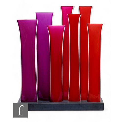 Rachel Woodman - A contemporary glass piece titled Vertical No 28, comprising seven blown and polished glass compressed sleeve form tubes in tonal reds and pinks mounted to a black slate base, signed to the reverse and dated 2004, height 78cm, width 65cm.