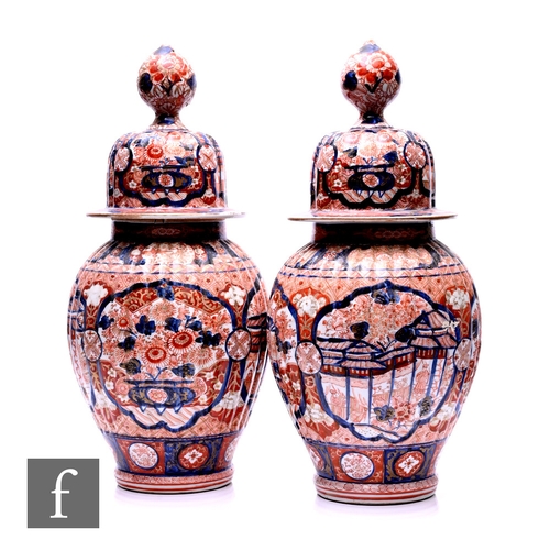 492 - A pair of Japanese 19th Century Imari vases and covers, each of fluted ribbed form, the ovoid bodies... 