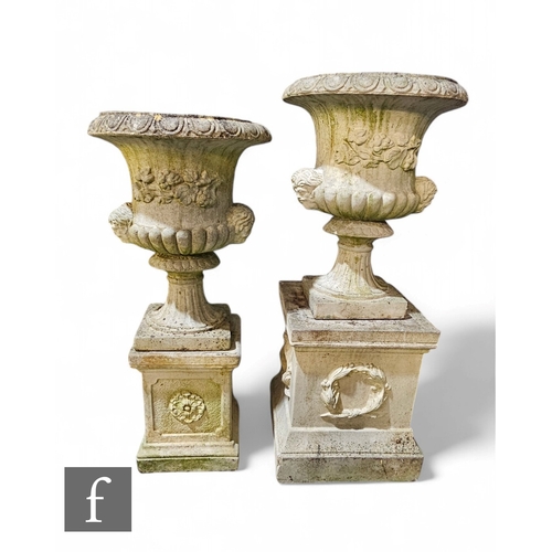 1115 - A near pair of composite stone terrace urns, each decorated with a floral border and double masks, o... 