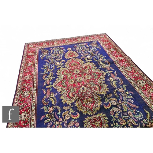 567 - A large Persian Qom style carpet, the central dark blue ground, detailed with arabesque floral motif... 