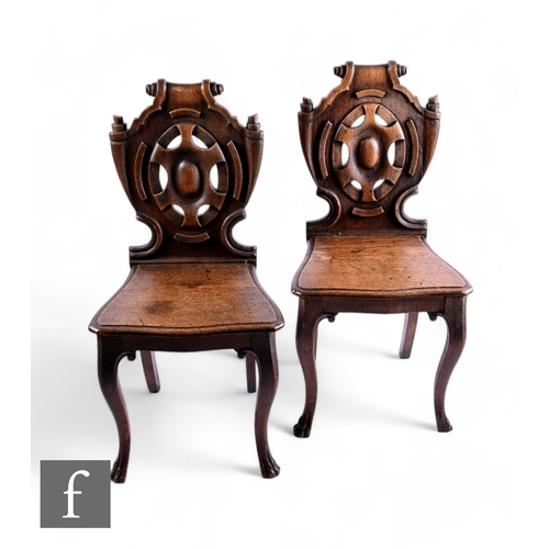 1037 - A pair of mid 19th Century carved oak Irish hall chairs, the scroll shield shaped backs over plank s... 