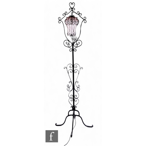 1093 - A wrought iron standard lamp with pink bubble glass shade suspended in a cartouche frame on scroll b... 