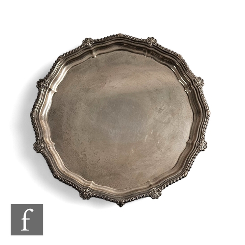 451 - A silver salver with scalloped shell and gadroon border and raised to four claw and ball feet, diame... 