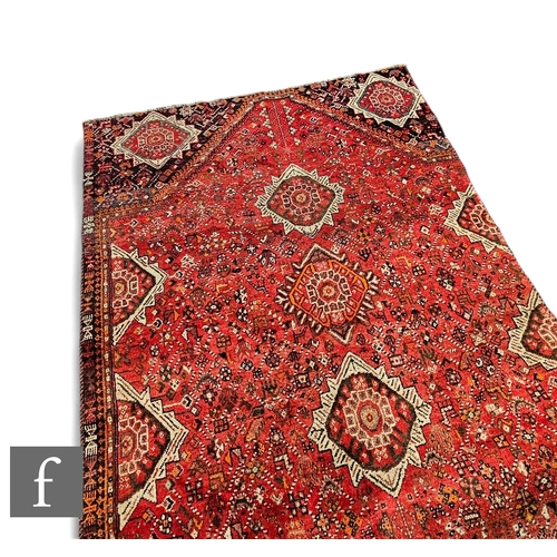 566 - A Persian wool Qashqai type rug, the red ground with a series of geometric designs and black corner ... 