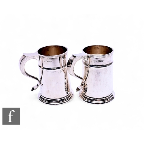 519 - A pair of 1930s silver half pint tankards in the Georgian style, each with a ribbed body and foot an... 