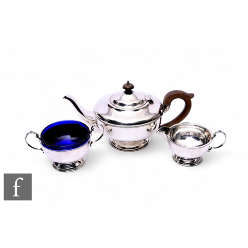 429 - A George V three-piece silver teaset, of plain form, teapot with wooden handle, sugar with blue glas... 