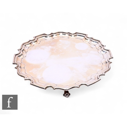 A hallmarked silver salver, with pie crust rim on three scroll feet ...