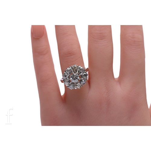 5 - A diamond cluster ring, the central brilliant-cut diamond high claw set within a bezel of nine brill... 