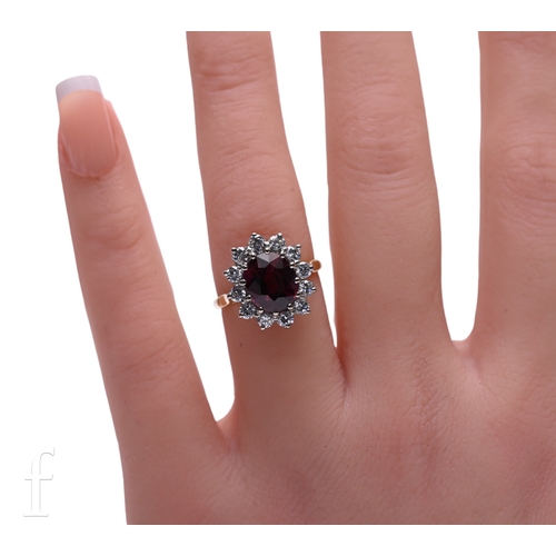 13 - A ruby and diamond cluster ring, the oval mixed-cut ruby twelve claw set within a bezel of brilliant... 