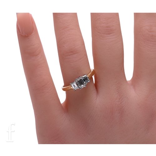 18 - A three stone diamond ring, the graduating emerald-cut diamonds claw set above plain band, hallmarke... 