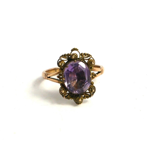 64 - AN EARLY 20TH CENTURY YELLOW METAL AND AMETHYST RING
The central oval cut stone set in a filigree mo... 