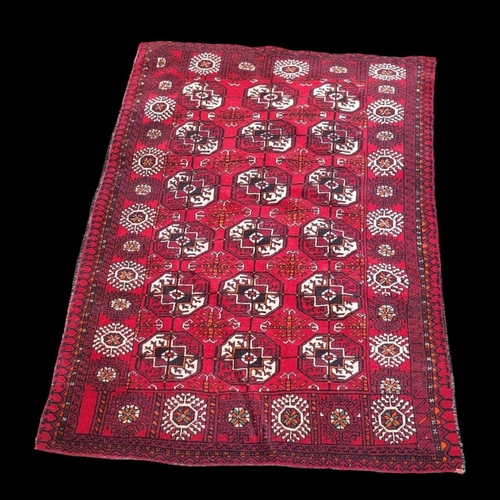 594 - A VINTAGE WOOLEN TRIBAL BOKHARA RUG
On red ground.
(115cm x 165cm)

Condition: good overall